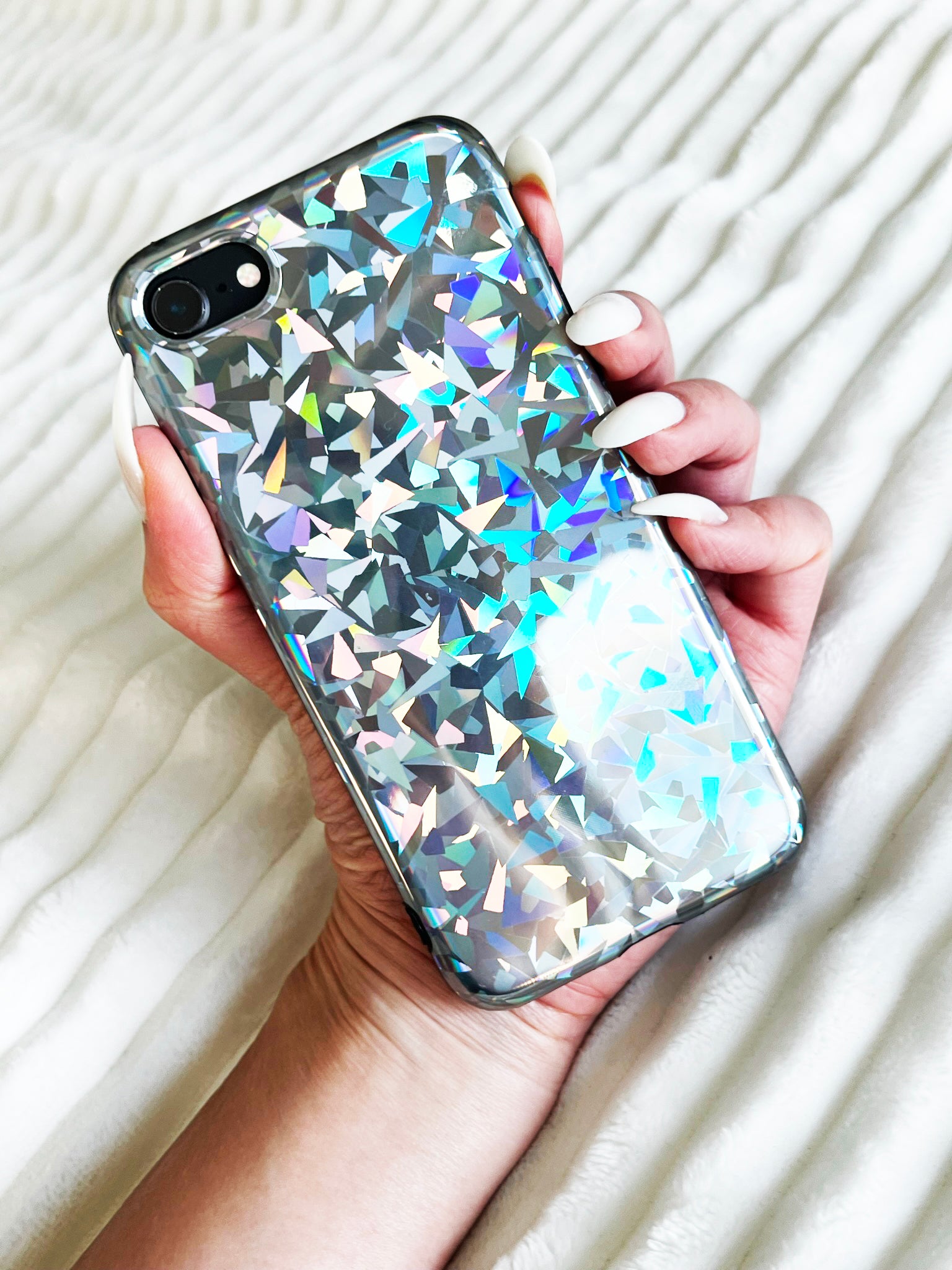 Holding up KokoLoveCo Laser Focus iPhone Case super shiny and colorful, on top of a white fluffy texture blanket